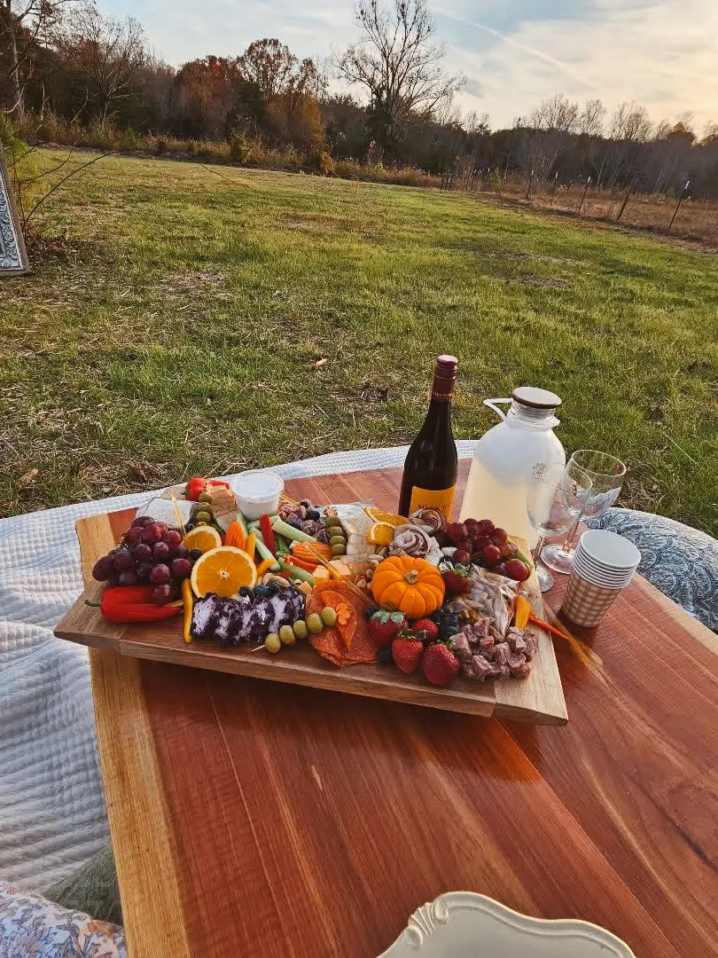 A charcuterie grazing board with wine, fresh fruits, meats, and cheeses on a wooden tray at an outdoor Magnolia Hill picnic