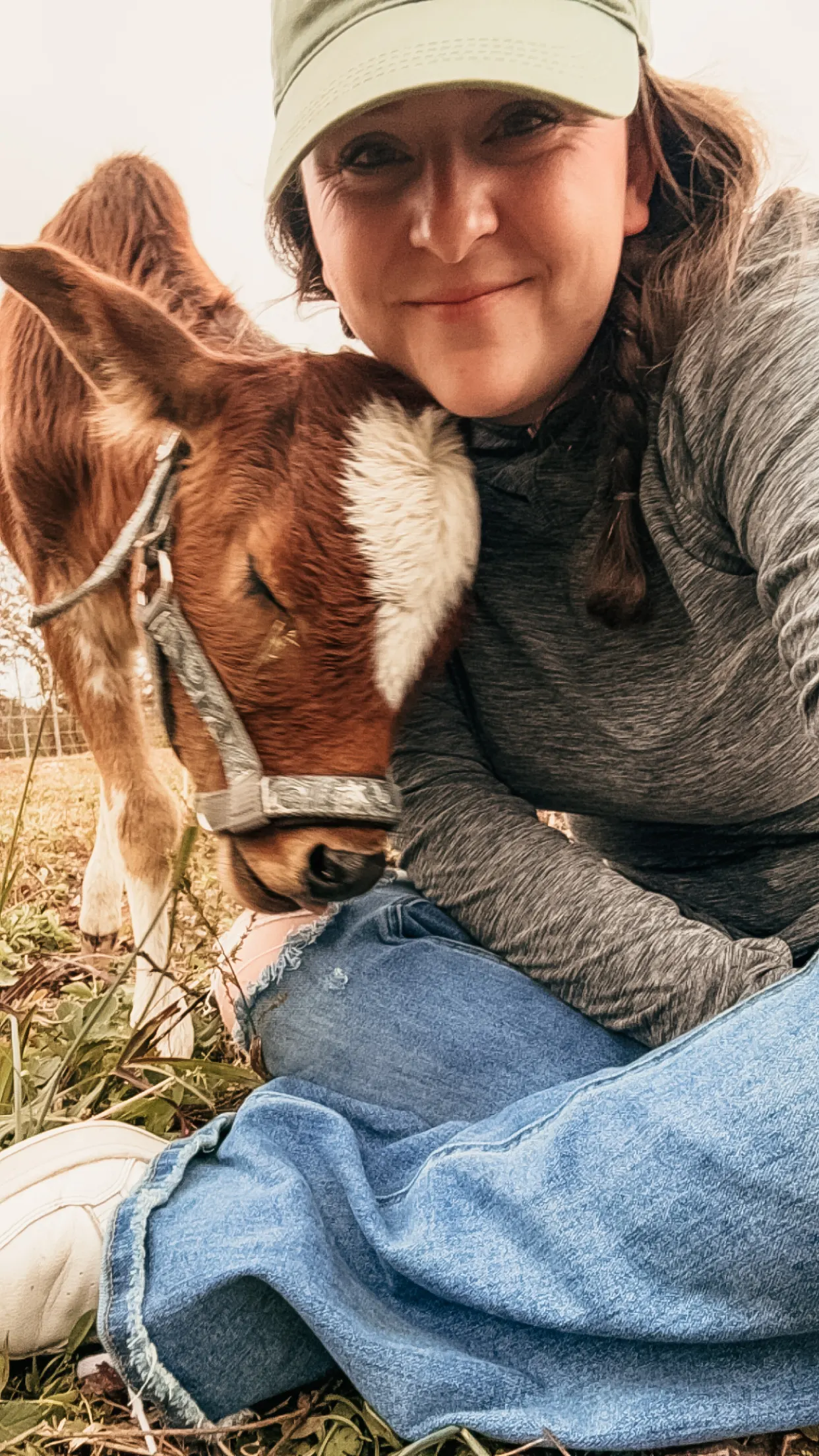 A woman kneeling in a field and nuzzling a young brown calf at Magnolia Hill