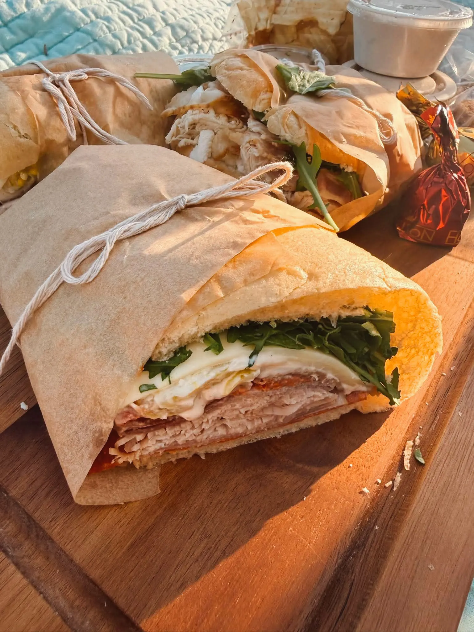 Artisan sandwiches wrapped in kraft paper and twine, sliced to reveal layers of turkey, arugula, and cheese