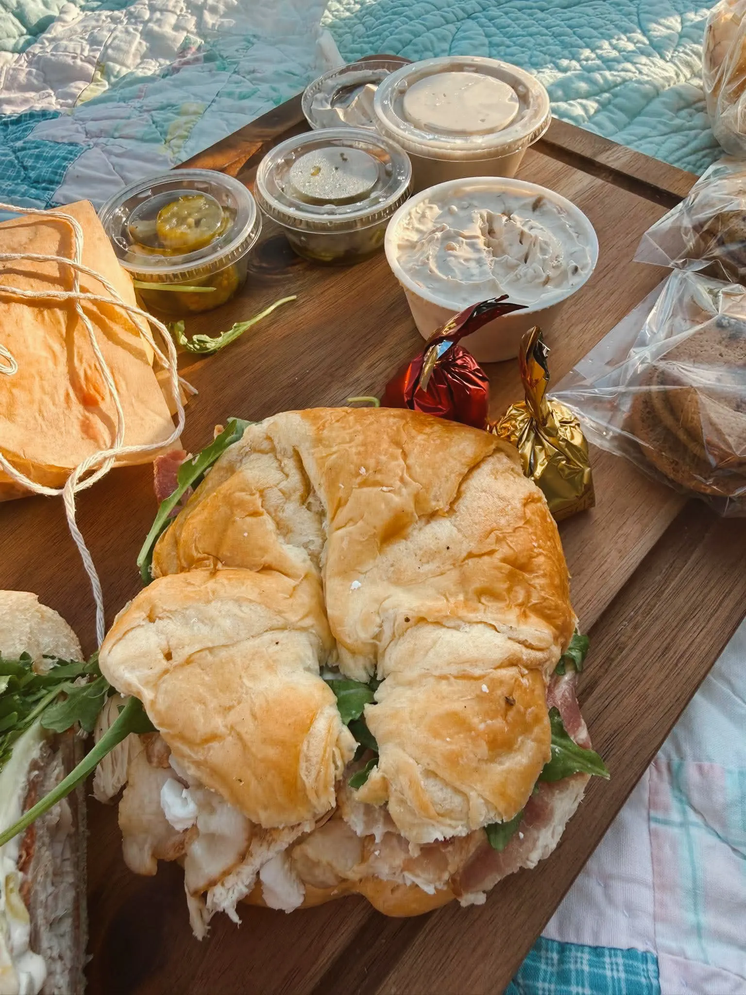 A croissant sandwich filled with chicken salad and arugula on a wooden board with dipping cups