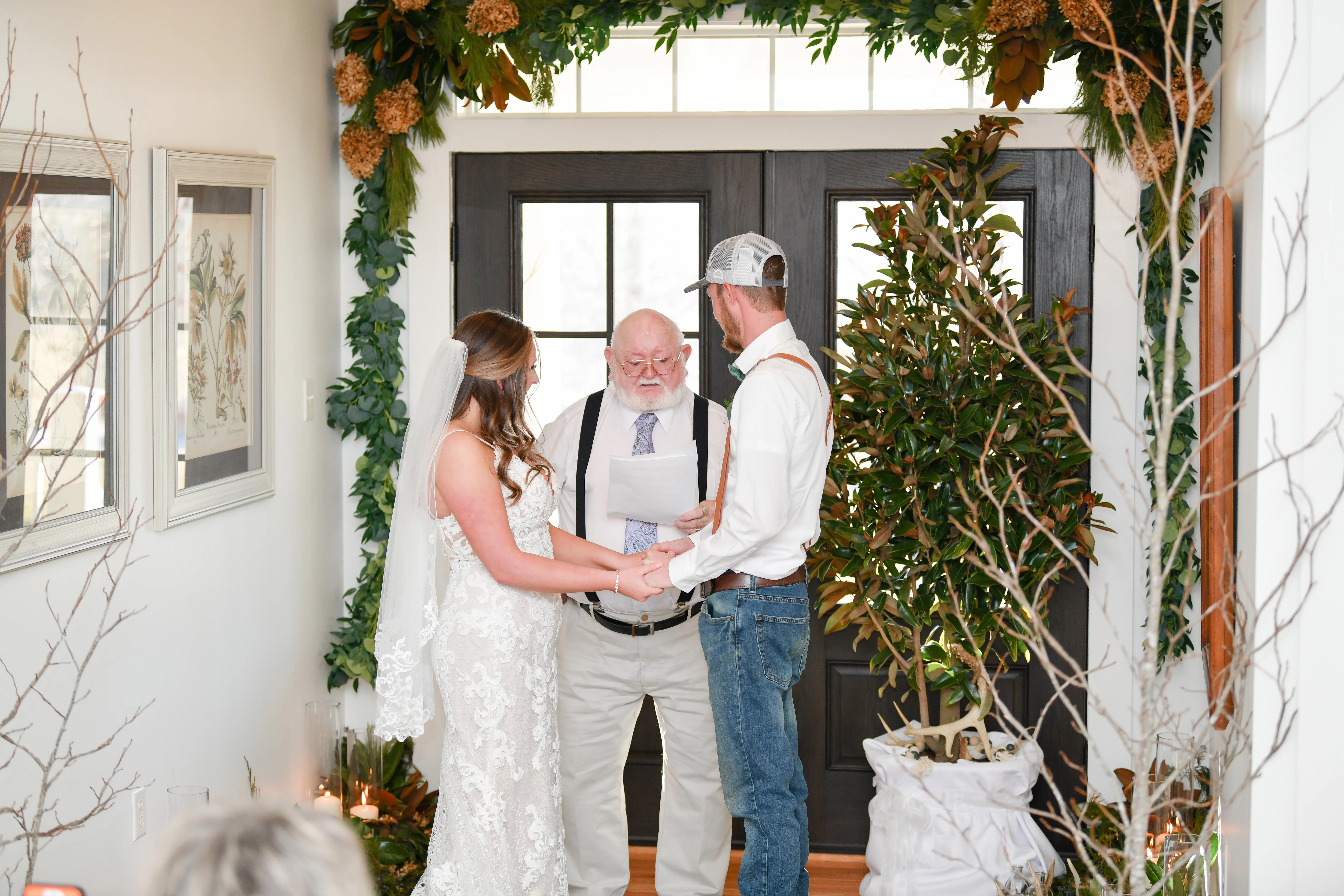 A wedding ceremony at Magnolia Hill, bride and groom holding hands beneath a greenery and floral archway